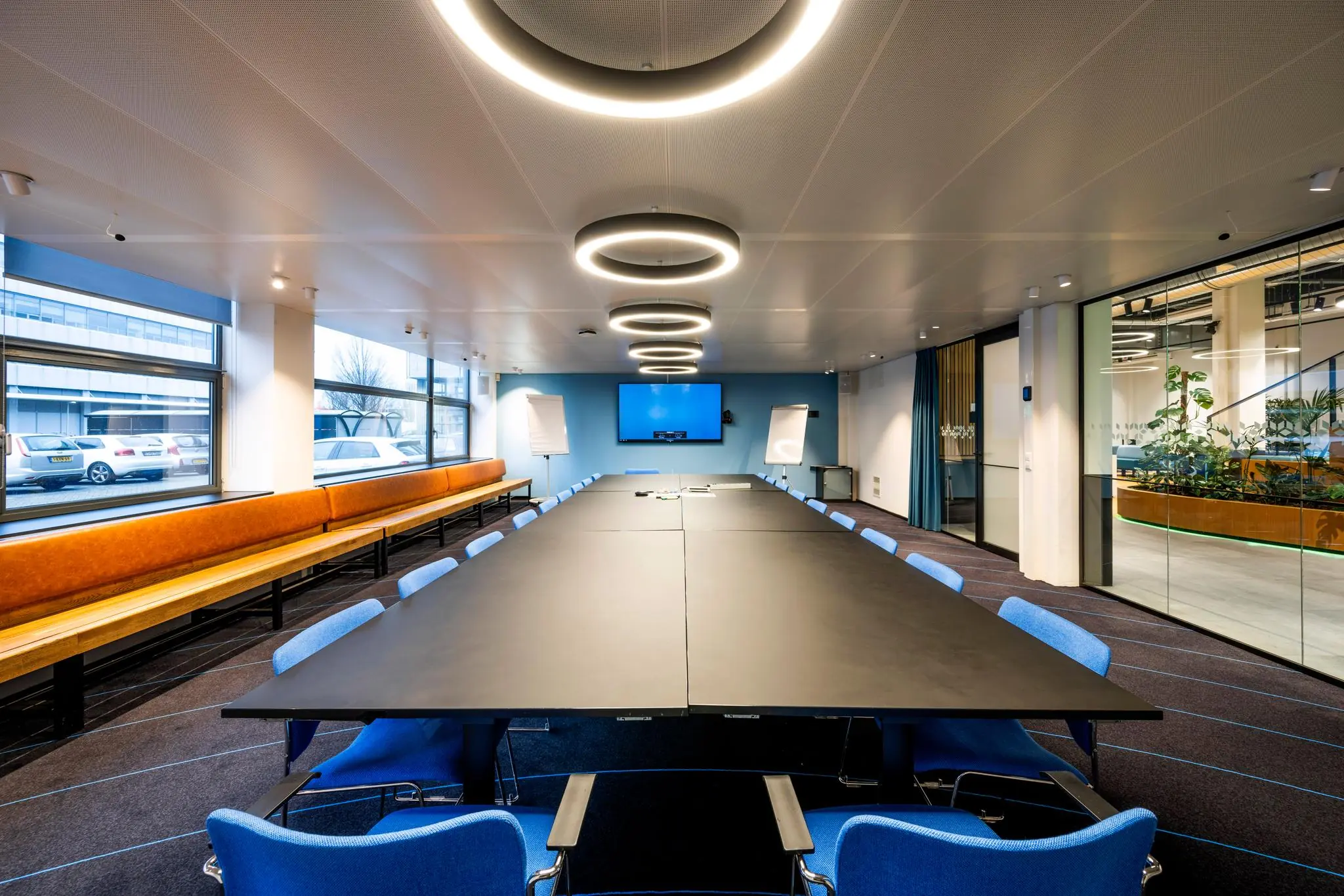 Moderne vergaderruimte aan de Kabelweg met lange tafel, blauwe stoelen, presentatieschermen en grote ramen.