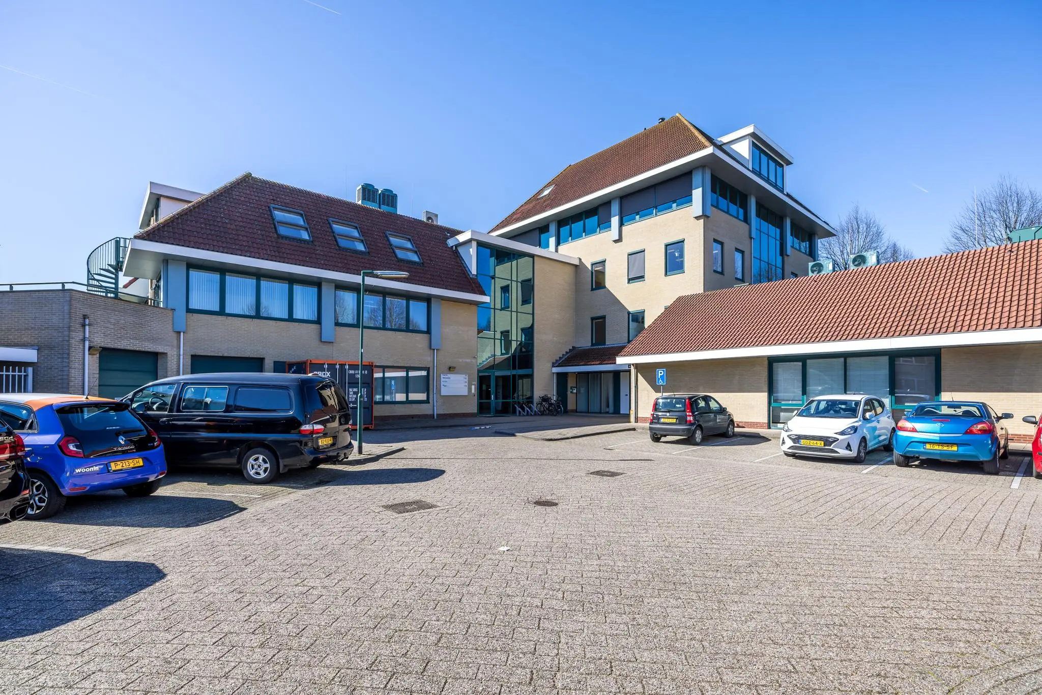Kantoor- en parkeergebouw aan de Dorpsstraat met geparkeerde auto's op een zonnige dag.