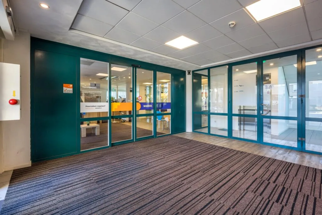 Ingang van het kantoor van woonin Dordt aan de Dorpsstraat, met glazen schuifdeuren en wachtruimte zichtbaar.