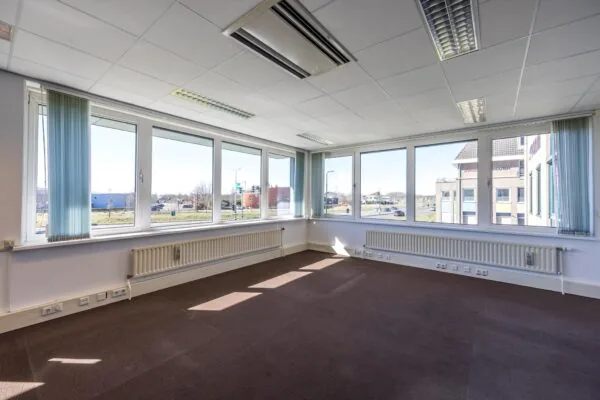 Lichte, lege kantoorruimte op de hoek van een gebouw aan de Dorpsstraat met grote ramen en uitzicht op de weg.