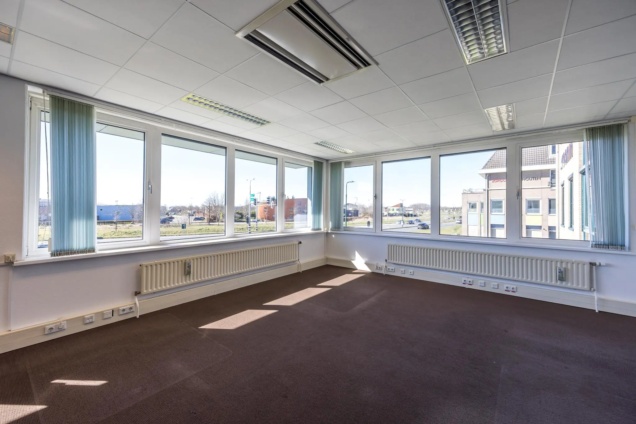 Lichte, lege kantoorruimte op de hoek van een gebouw aan de Dorpsstraat met grote ramen en uitzicht op de weg.