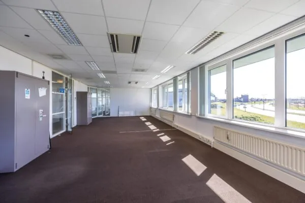 Licht en ruim leegstaand kantoorpand aan de Dorpsstraat met grote ramen en bruin tapijt.