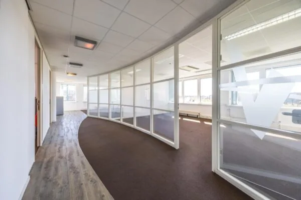 Lichte kantoorruimte aan de Dorpsstraat met glazen scheidingswanden en gebogen gangpad.