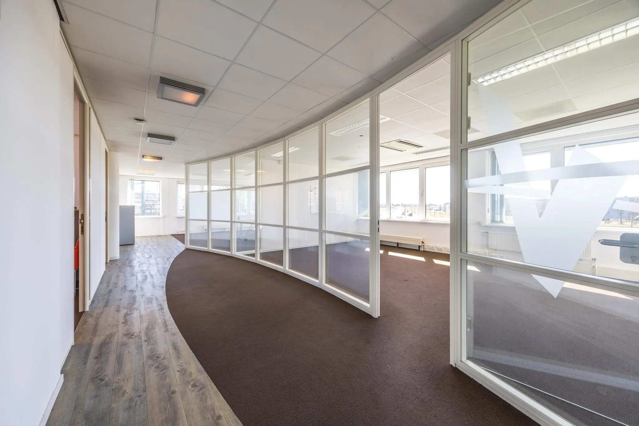 Lichte kantoorruimte aan de Dorpsstraat met glazen scheidingswanden en gebogen gangpad.
