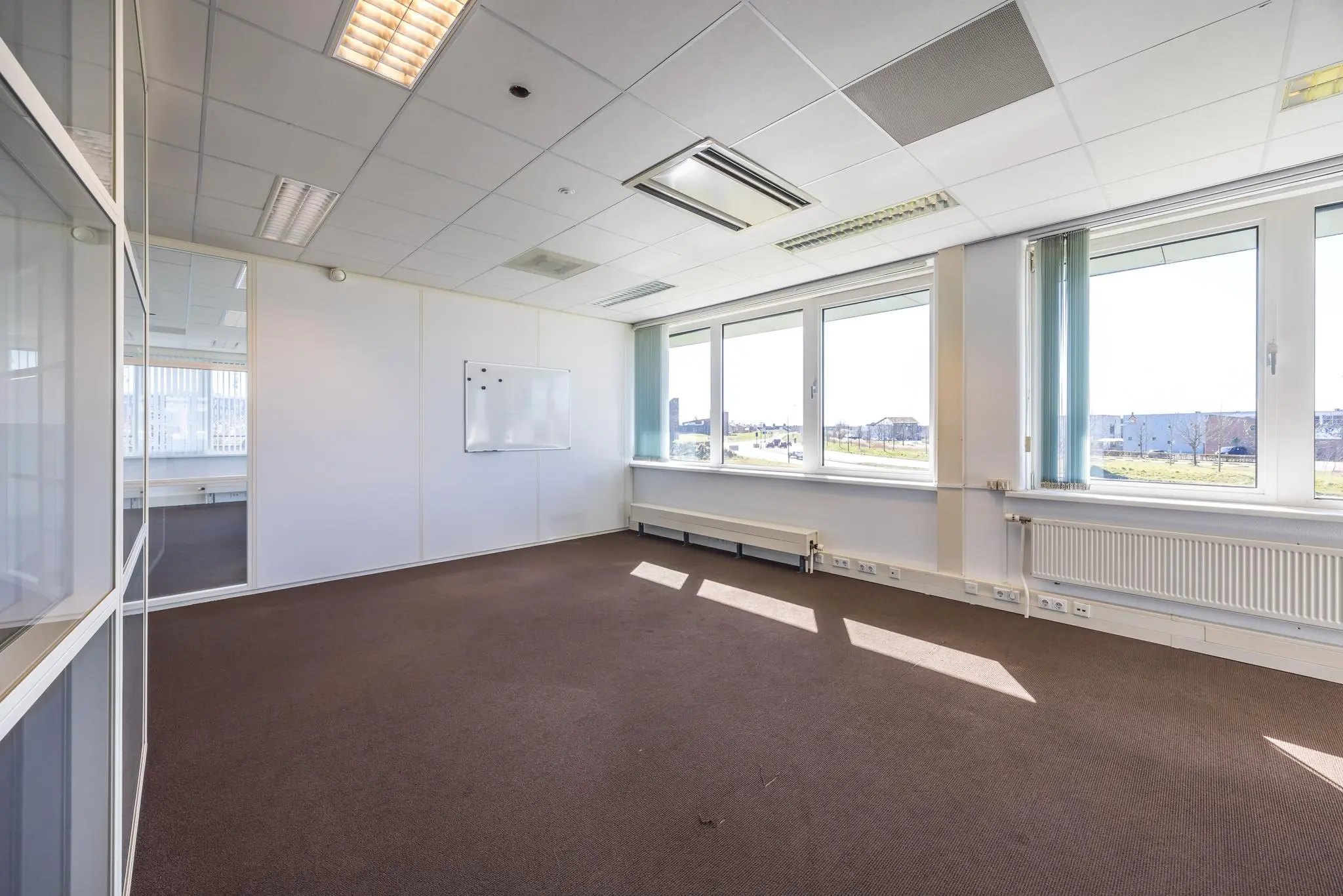 Lichte, lege kantoorruimte aan de Dorpsstraat met grote ramen en een whiteboard aan de muur.