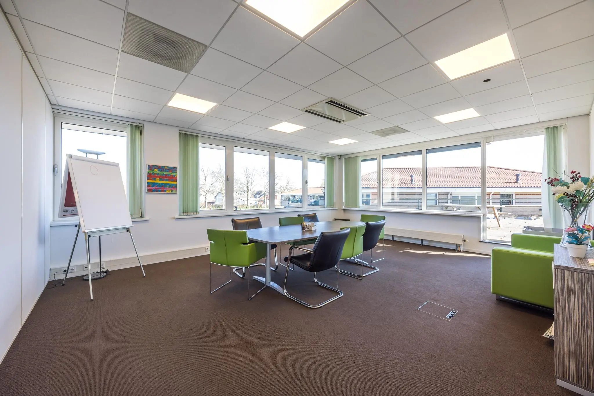 Vergaderruimte met moderne inrichting, grote ramen en een flip-over in een kantoor aan de Dorpsstraat.