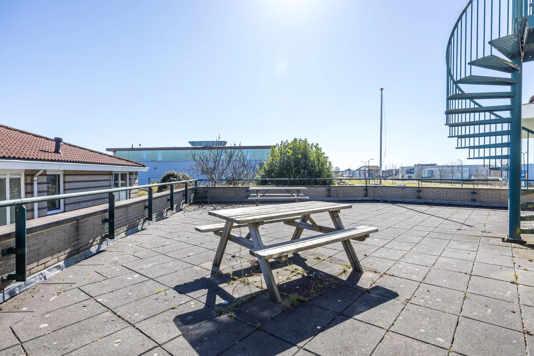 Zonnig dakterras aan de Dorpsstraat met picknicktafels en metalen wenteltrap.