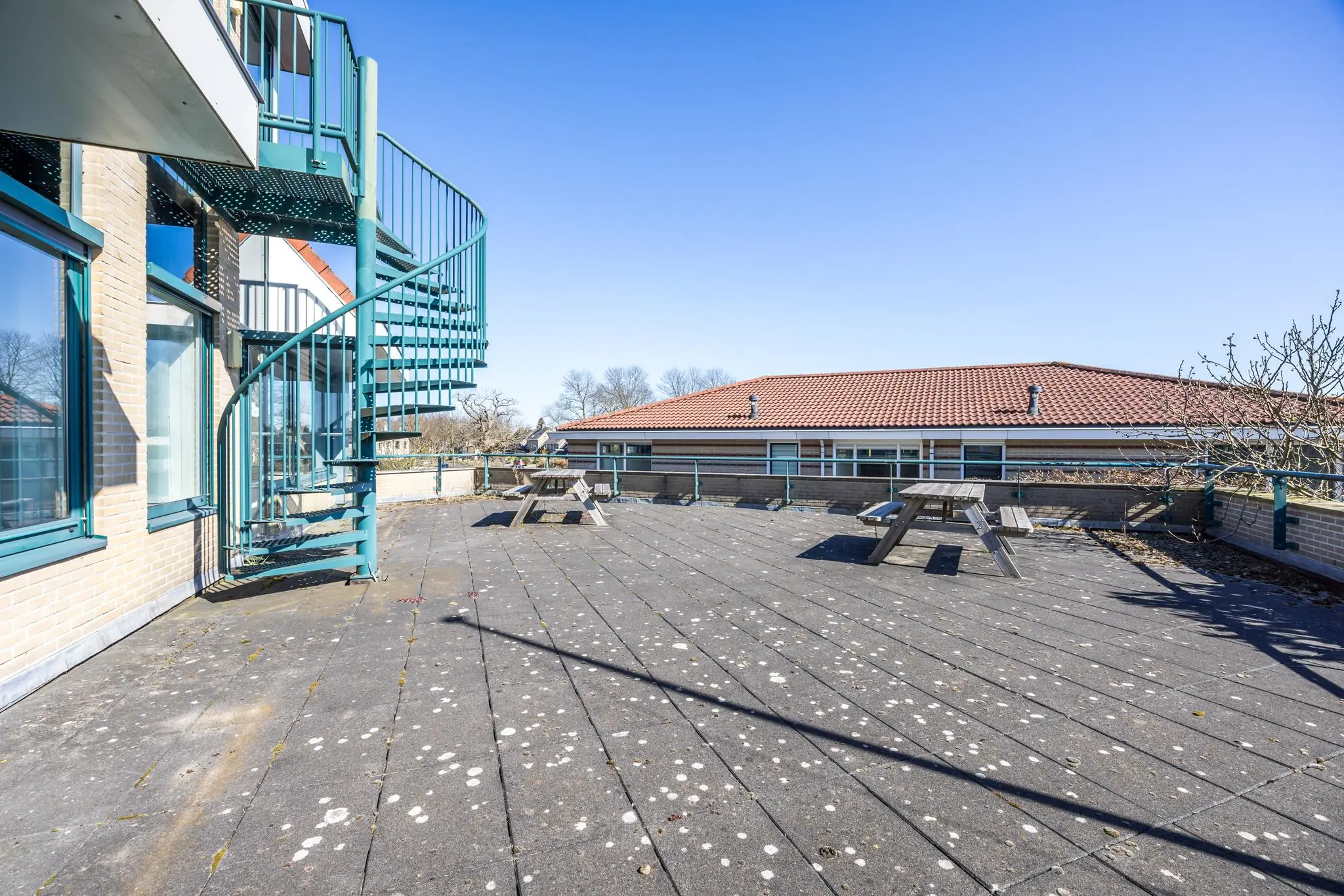 Ruim dakterras aan de Dorpsstraat met picknicktafels en een groene wenteltrap, onder een heldere blauwe lucht.