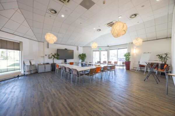 Vergaderruimte aan de Dorpsstraat met opgestelde tafels en stoelen, een groot presentatiescherm, flip-over en veel daglicht.