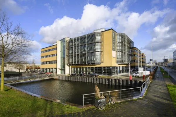 Modern kantoorgebouw aan de H.J.E. Wenckebachweg in Amsterdam met waterpartij op de voorgrond en opvallende gevel met horizontale lamellen.