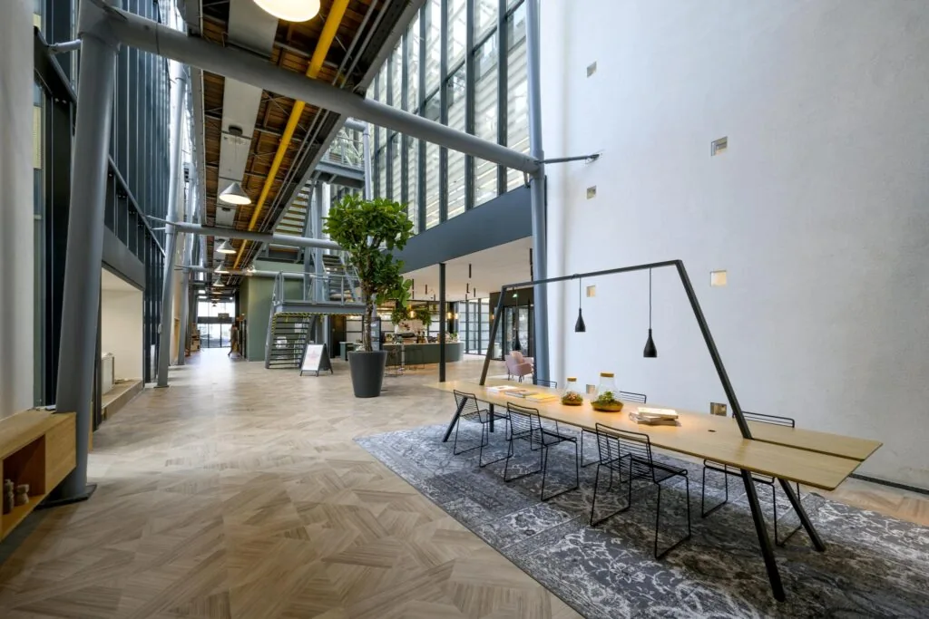 Moderne, ruimtelijke kantoorlobby aan de H.J.E. Wenckebachweg met hoge plafonds, grote ramen, een lange vergadertafel en industriële details.