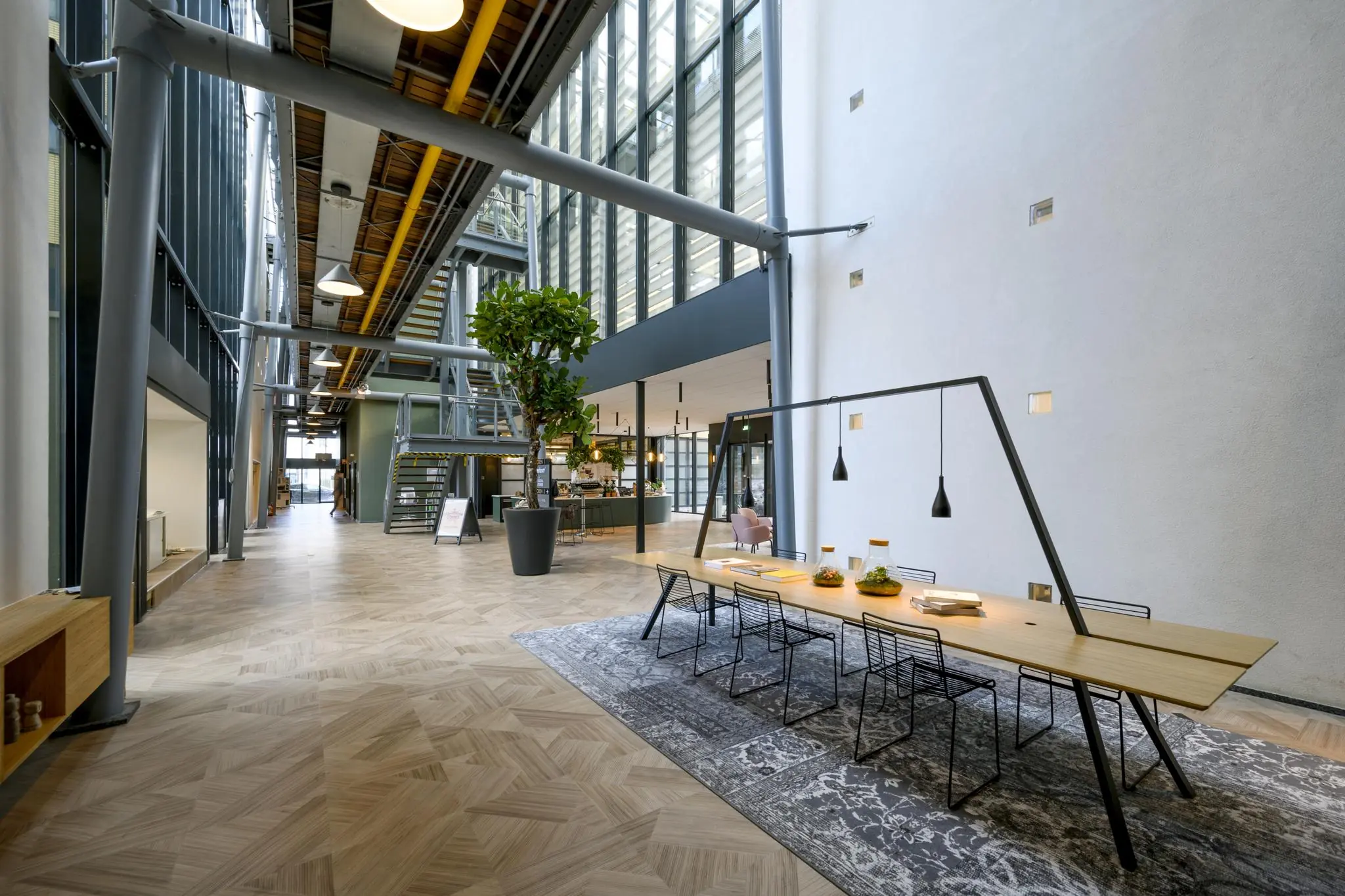 Moderne, ruimtelijke kantoorlobby aan de H.J.E. Wenckebachweg met hoge plafonds, grote ramen, een lange vergadertafel en industriële details.