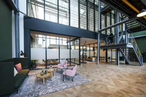 Moderne kantoorlobby aan de H.J.E. Wenckebachweg met glazen vergaderruimtes, zithoek en open trap.
