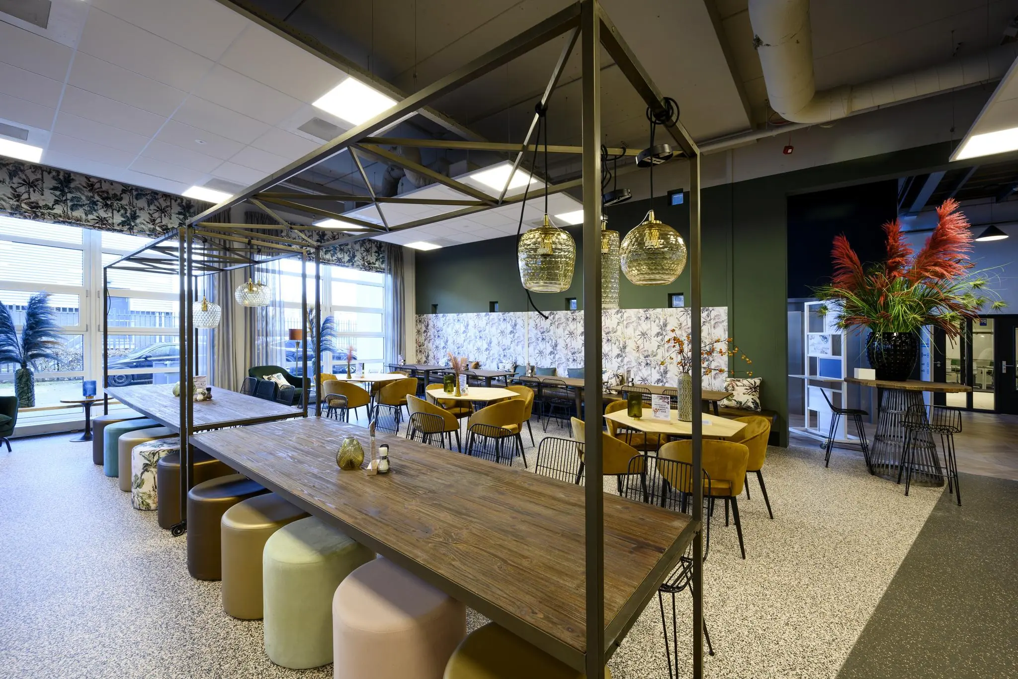 Modern ingericht bedrijfsrestaurant aan de H.J.E. Wenckebachweg met lange houten tafels, kleurrijke stoelen en decoratieve verlichting.