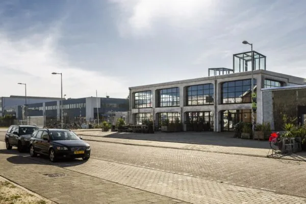 Industrieel pand aan het Gedempt Hamerkanaal met grote ramen en geparkeerde auto's op de voorgrond.