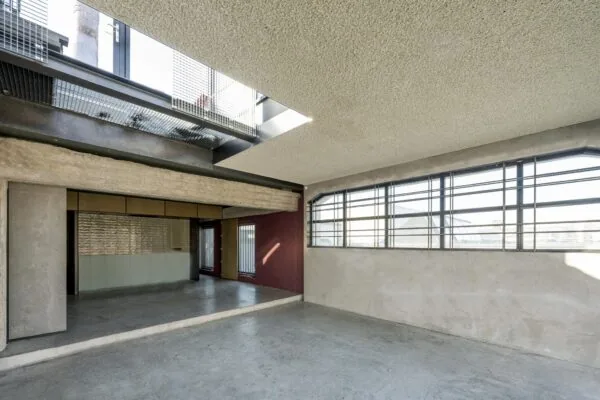 Binnenruimte van een industrieel gebouw aan het Gedempt Hamerkanaal met betonnen vloeren, metalen raamkozijnen en een open plafond met roosterplaten.