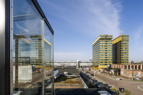 Twee gouden woontorens aan het Gedempt Hamerkanaal in Amsterdam-Noord met industriële bebouwing op de voorgrond.