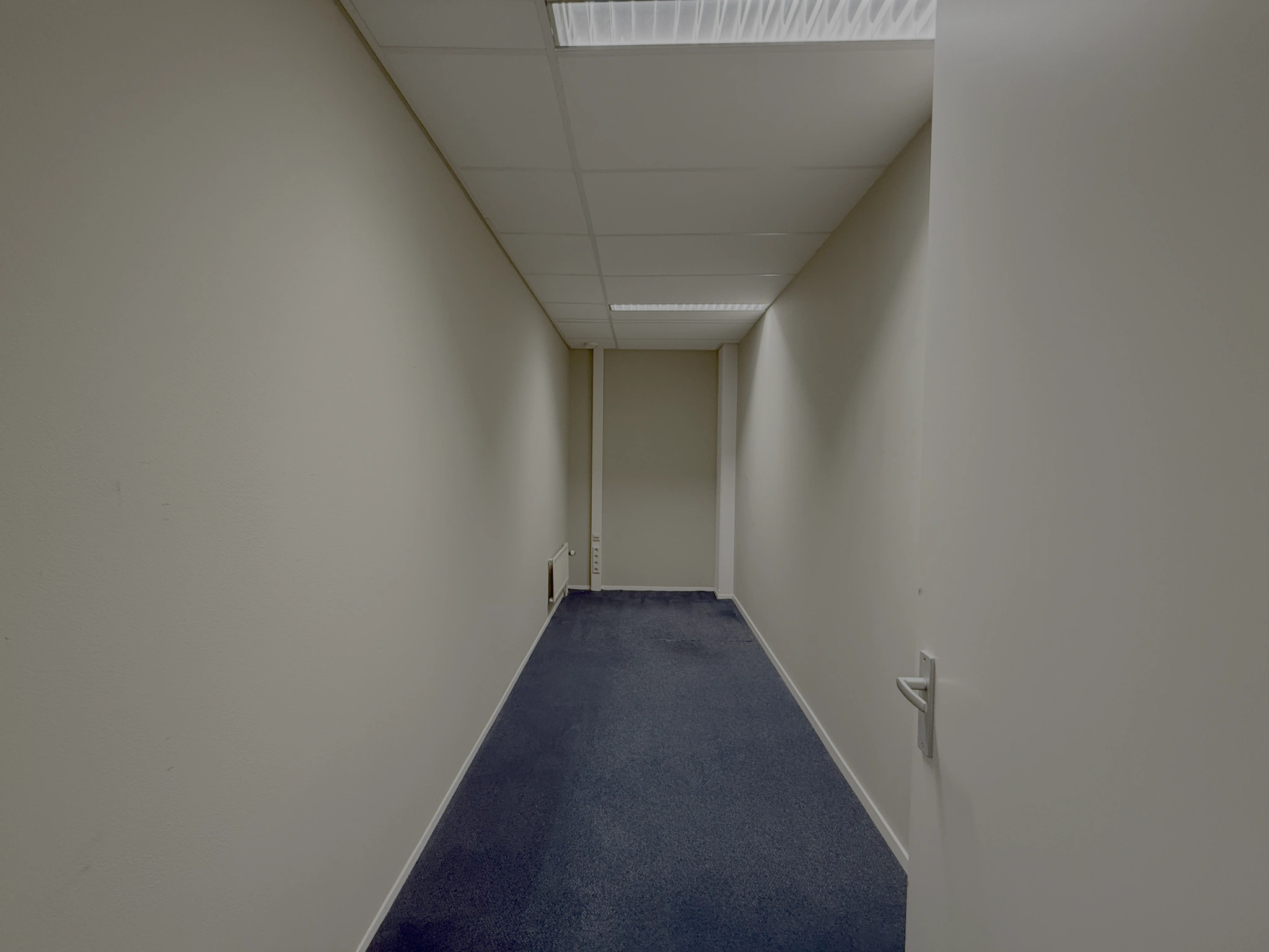 Een smalle, lege gang met beige muren en blauw tapijt in een kantoorgebouw aan de Lunettenbaan.