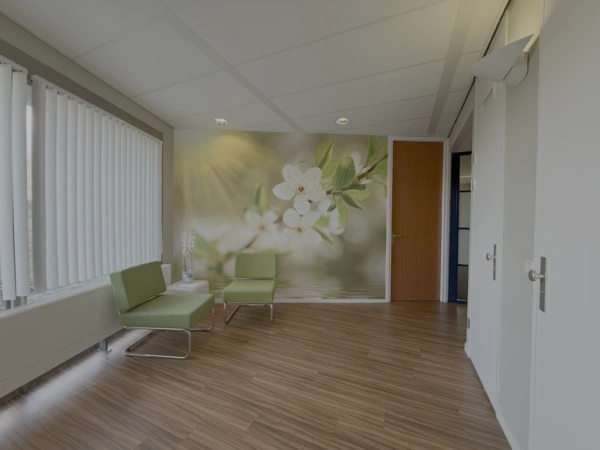 Wachtruimte met groene stoelen, houtkleurige vloer en een fotobehang van witte bloesem aan de Lunettenbaan.