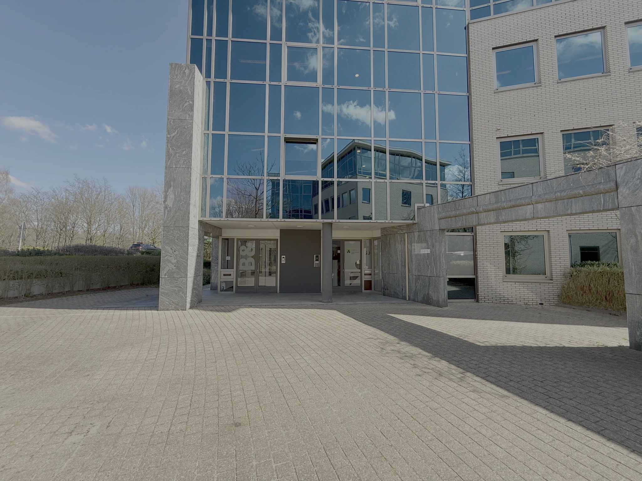 Ingang van een modern kantoorgebouw aan de Lunettenbaan met glazen gevel en marmeren accenten.