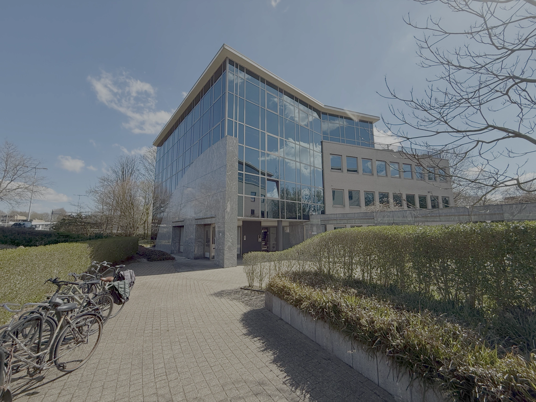 Kantoorgebouw aan de Lunettenbaan met glazen gevel en fietsenstalling op de voorgrond.