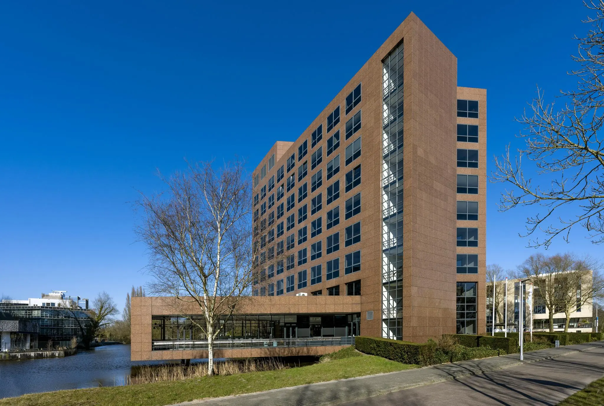 Modern kantoorgebouw aan de Prof. W.H. Keesomlaan met roodbruine gevel en grote ramen, gelegen aan het water.