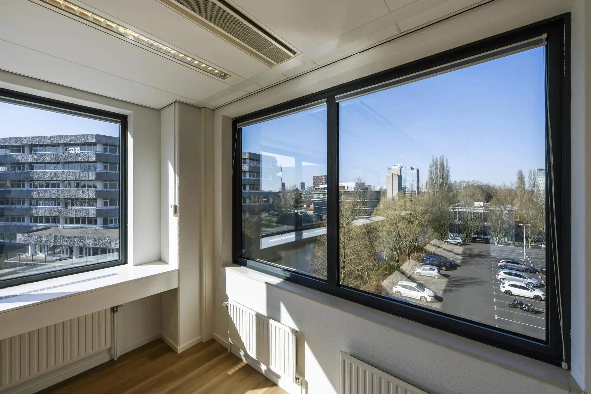 Uitzicht vanuit een kantoorpand aan de Prof. W.H. Keesomlaan op omliggende gebouwen, parkeerplaats en bomen.