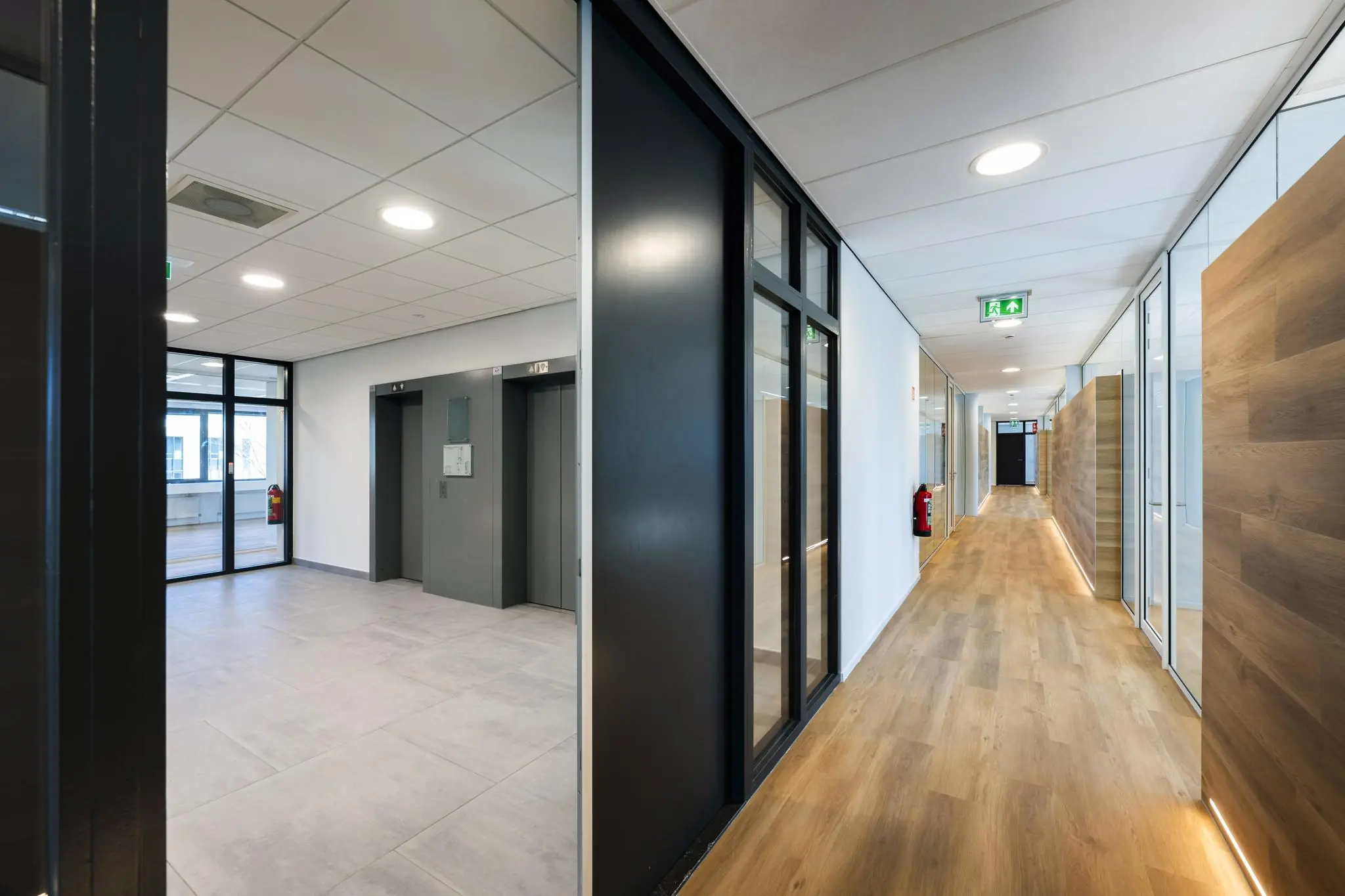 Moderne gang en lifthal in een kantoorpand aan de Prof. W.H. Keesomlaan met strakke afwerking en houten vloer.