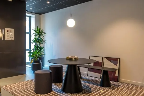 Moderne zithoek met een ronde zwarte tafel, minimalistische krukken, een hanglamp en planten in een strakke interieursetting.