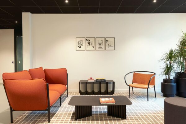 Moderne wachtruimte met oranje bank, designstoel, zwarte salontafel en abstracte kunst aan de muur.
