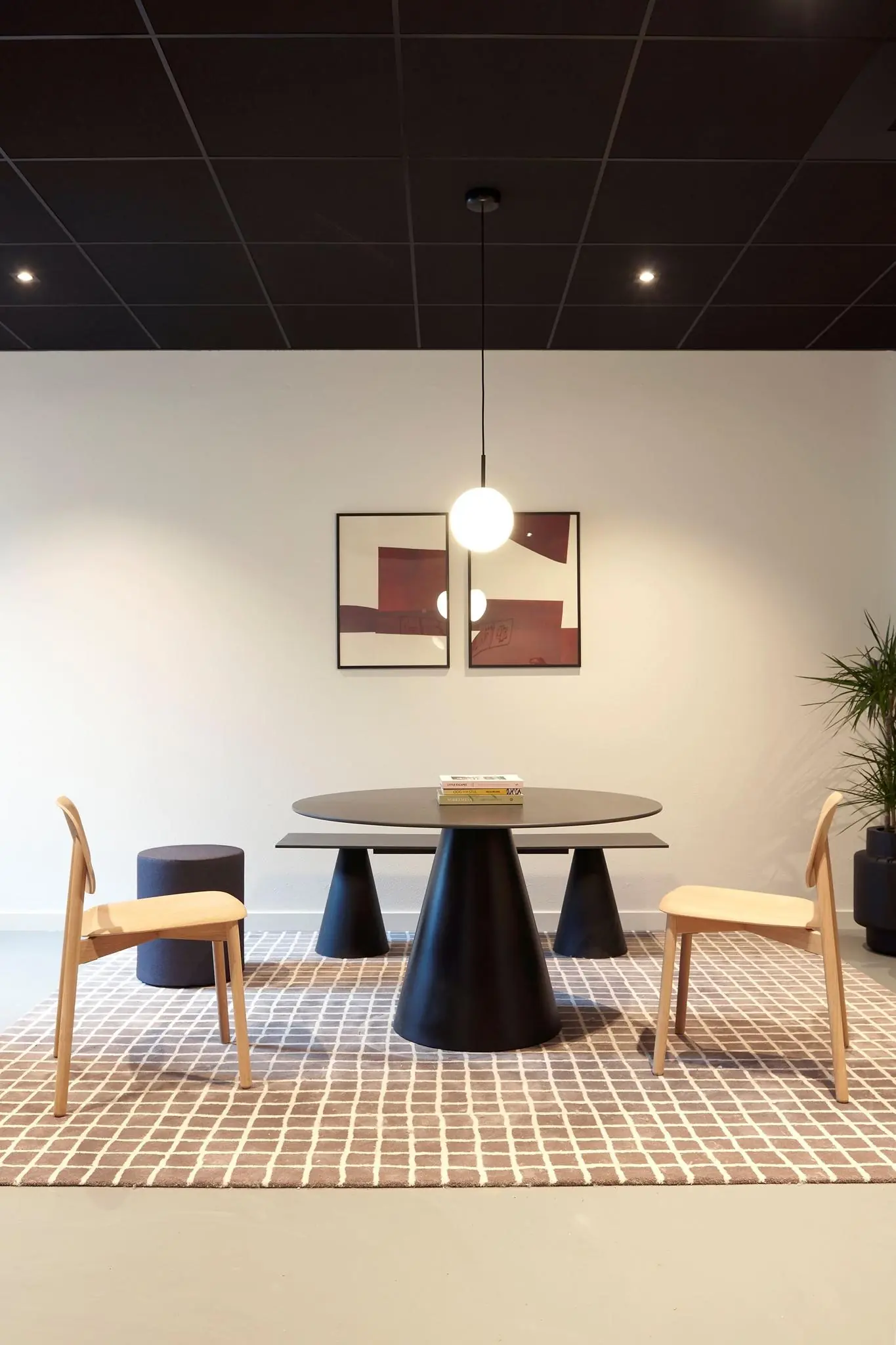 Modern ingerichte zithoek met een ronde zwarte tafel, houten stoelen, een grafisch vloerkleed en abstracte kunst aan de muur.