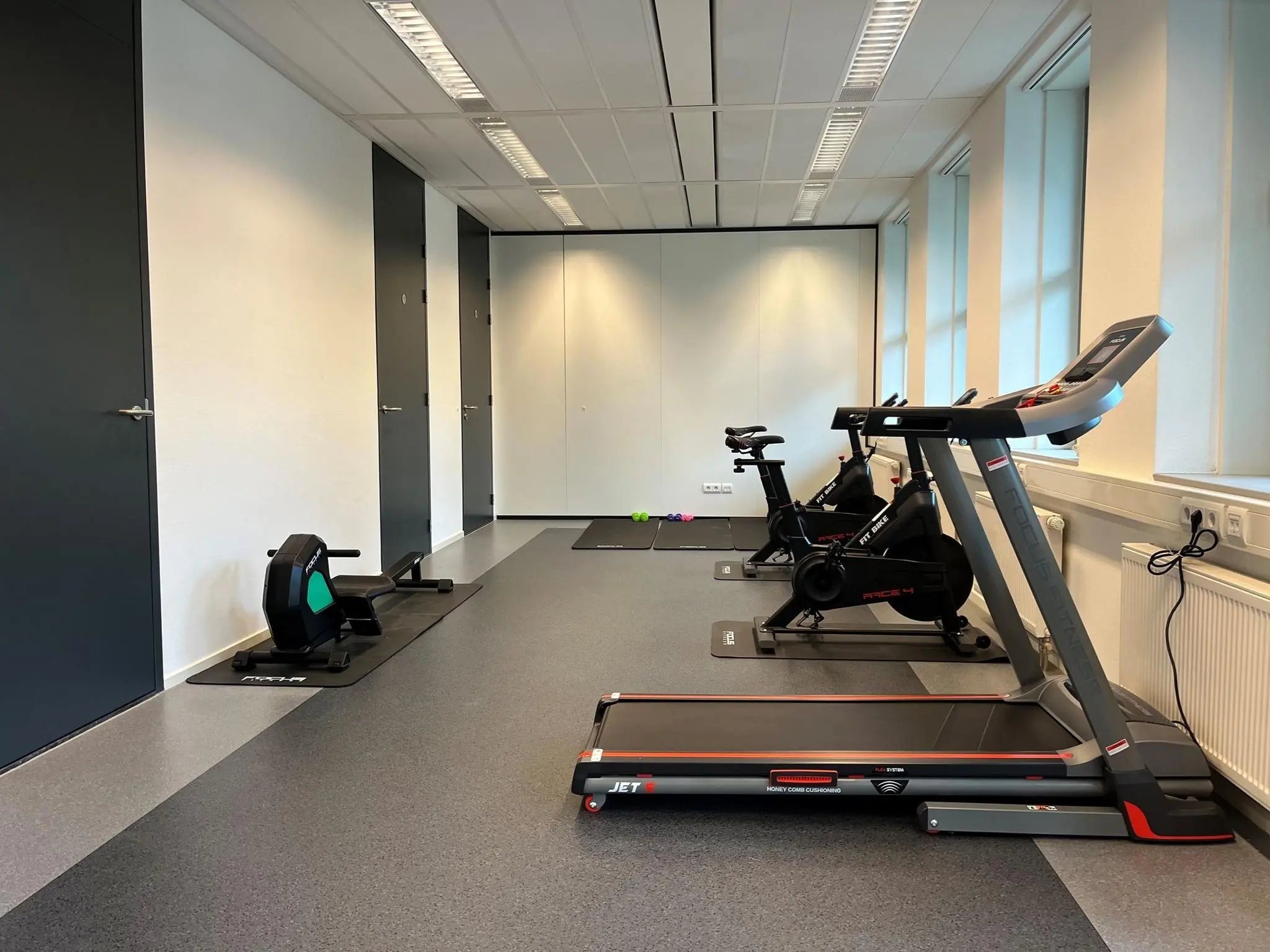 Fitnessruimte met een loopband, hometrainers en een roeimachine naast elkaar opgesteld.