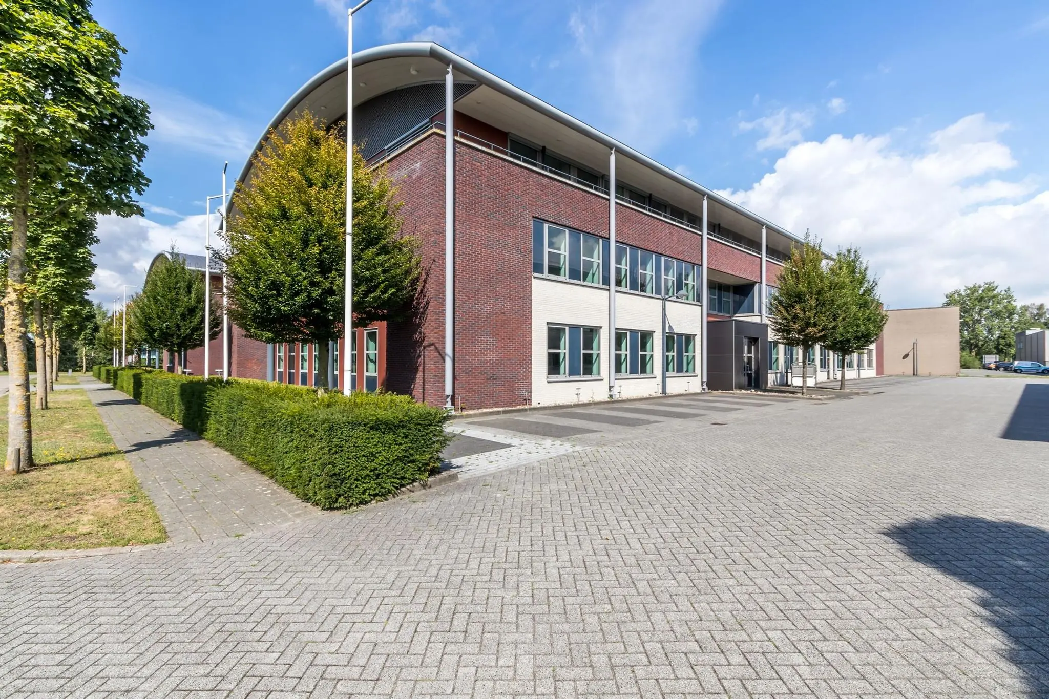 Modern bedrijfsgebouw aan de De Wel met rood-witte gevel en ruime bestrate parkeerplaats.