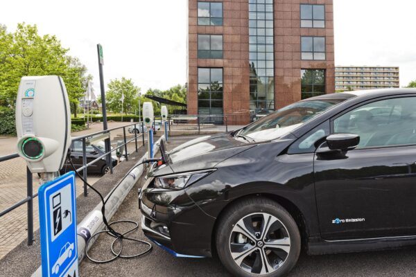 Zwarte elektrische auto laadt op bij een laadpaal op de Prof. W.H. Keesomlaan, naast een modern kantoorgebouw.