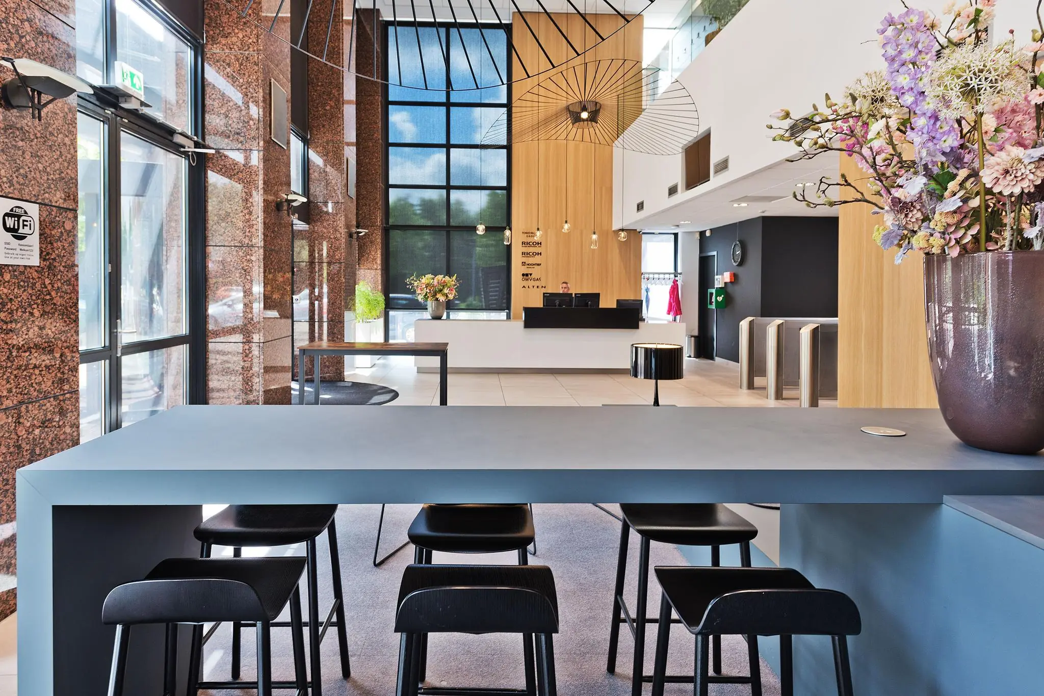 Moderne ontvangsthal aan de Prof. W.H. Keesomlaan met een balie, zitgedeelte en bloemdecoratie.