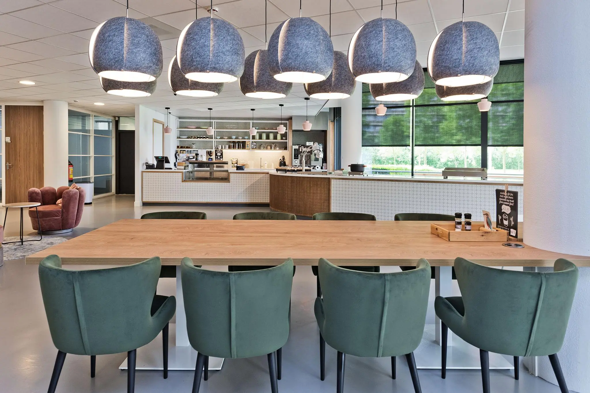 Moderne en lichte kantine met een lange houten tafel, groene stoelen en een open koffiekeuken aan de Prof. W.H. Keesomlaan.