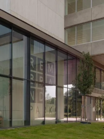 Glazen gevel van een modern kantoorgebouw aan de Nachtwachtlaan met de reflectie van het logo 'Rembrand Park'.