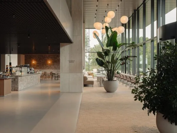 Moderne lobby aan de Nachtwachtlaan met grote raampartijen, een koffiebar en stijlvolle zitgelegenheden omringd door groene planten.