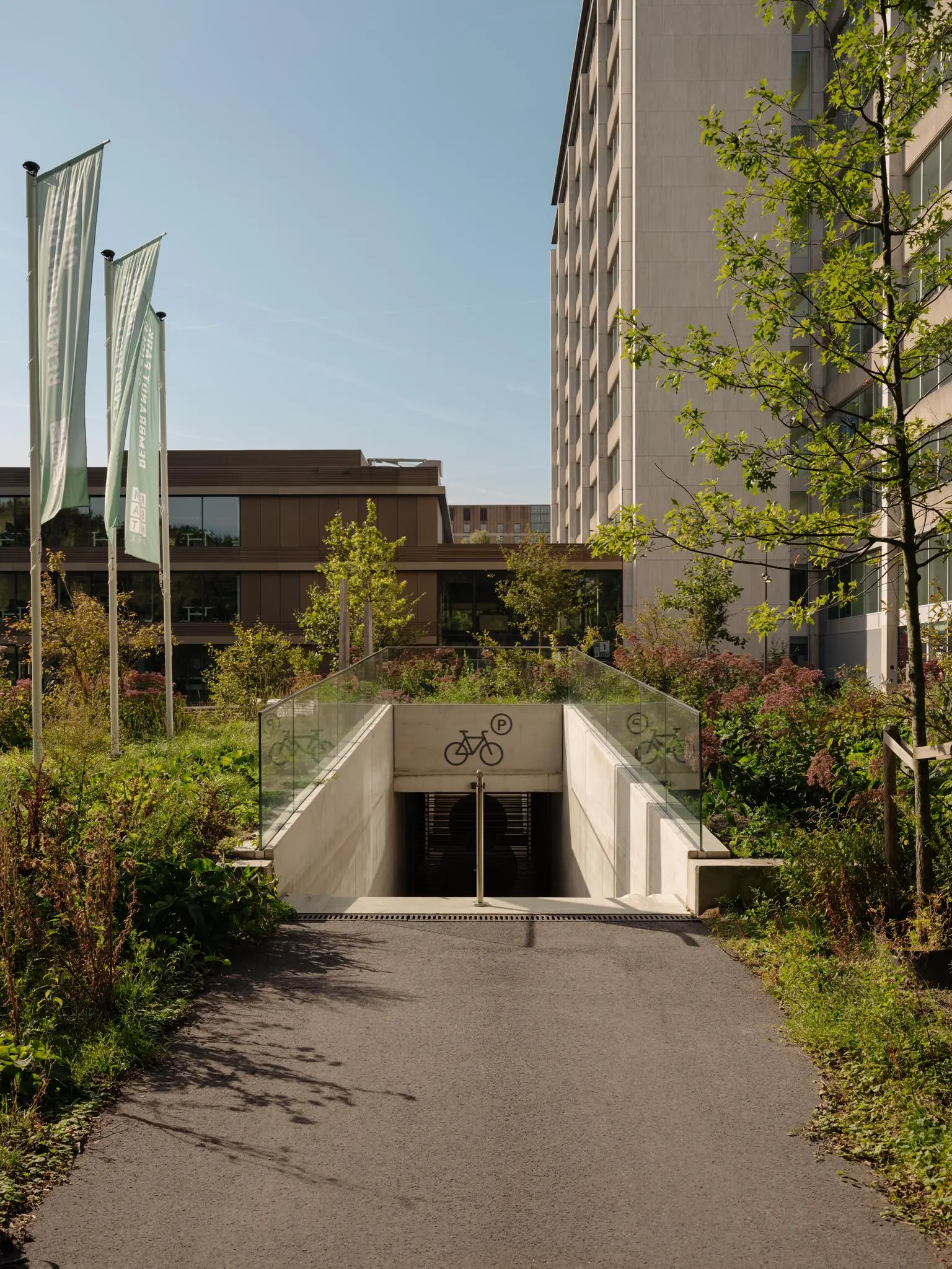 Ingang van een ondergrondse fietsenstalling aan de Nachtwachtlaan, omringd door groene beplanting en moderne gebouwen.