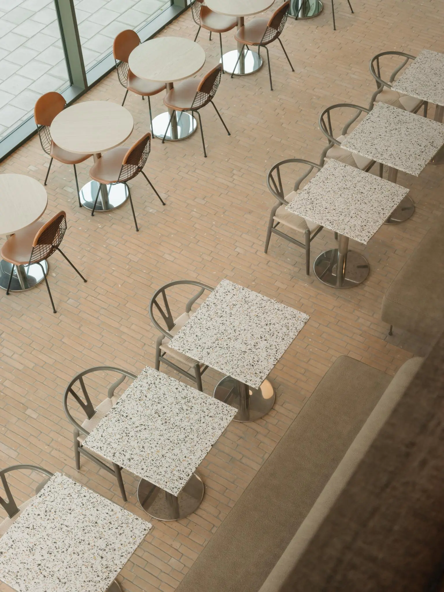 Overzicht van een modern horecagedeelte aan de Nachtwachtlaan met ronde en vierkante tafels en verschillende stoelen op een lichtbruine tegelvloer.