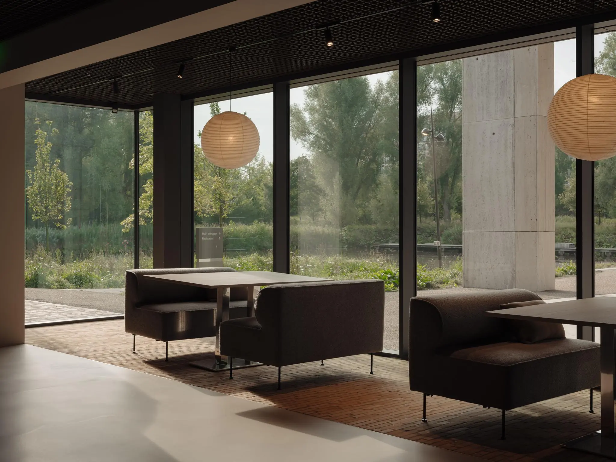 Moderne zithoek met donkergrijze banken en hanglampen aan de Nachtwachtlaan, met uitzicht op groen landschap door grote ramen.