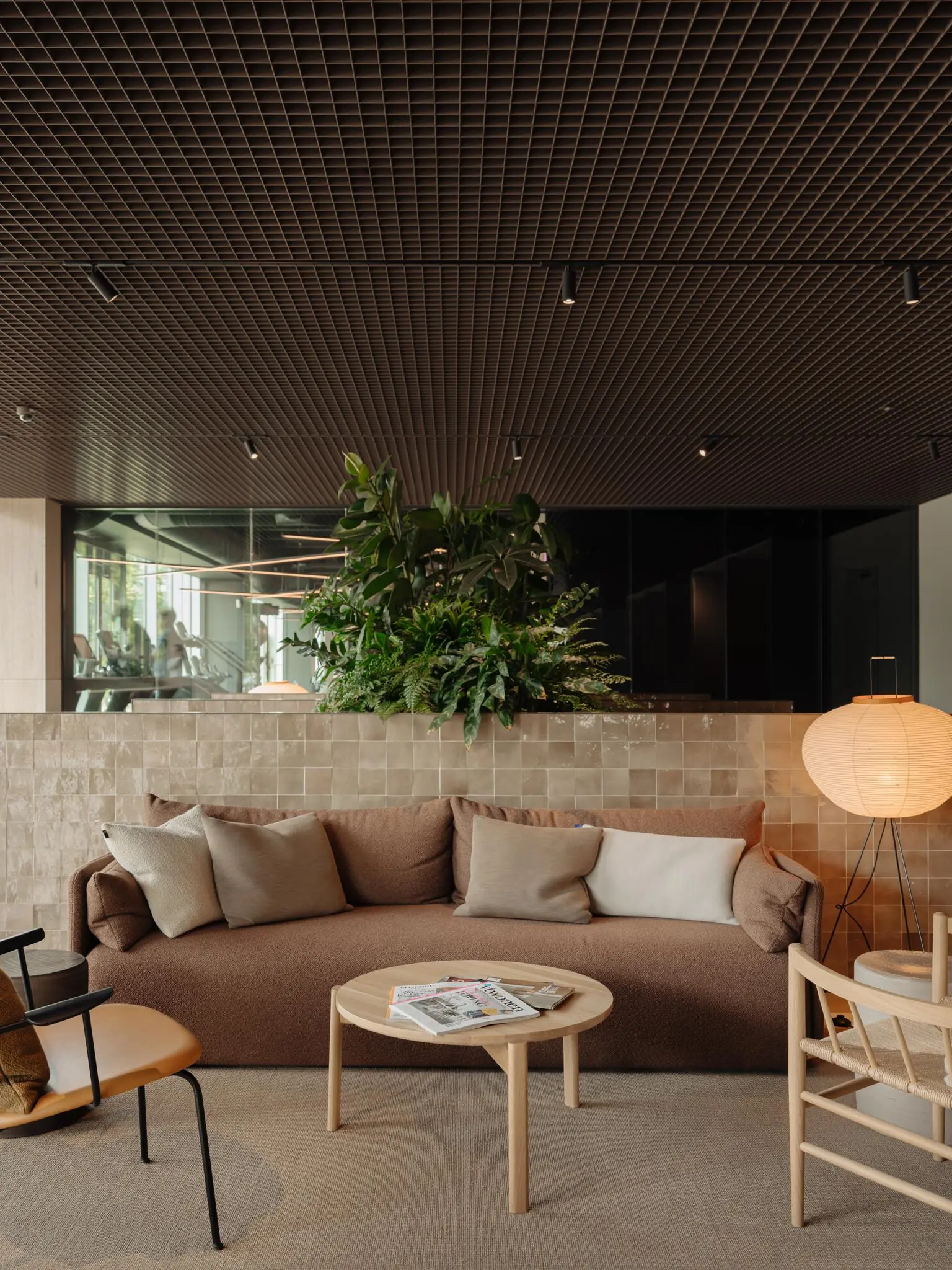 Moderne loungehoek aan de Nachtwachtlaan met een bruine bank, houten meubels, planten en warme verlichting.