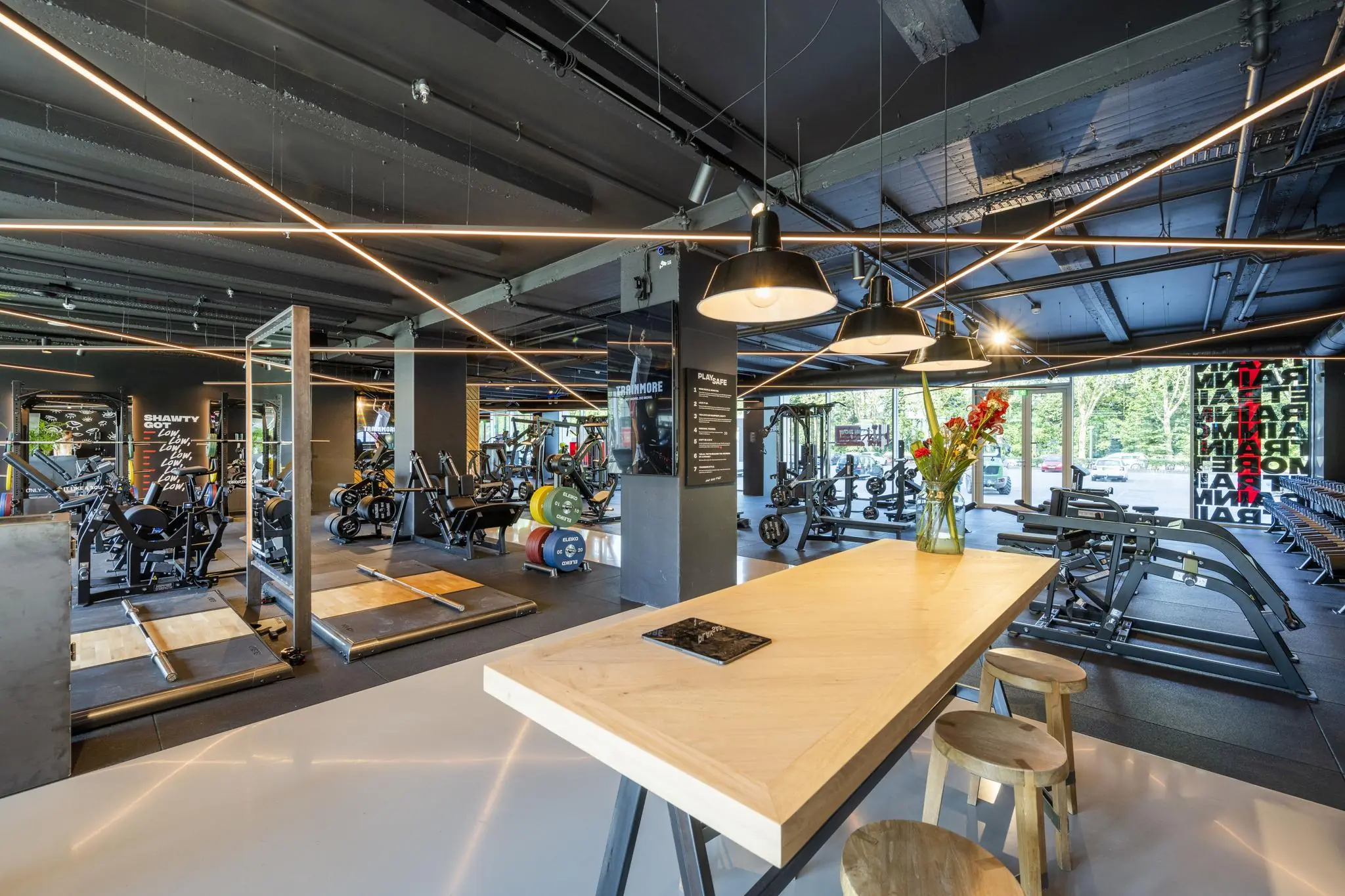 Moderne fitnessruimte aan de Nachtwachtlaan met krachttrainingsapparatuur, halterplatforms en een tafel met krukken en bloemenvaas op de voorgrond.