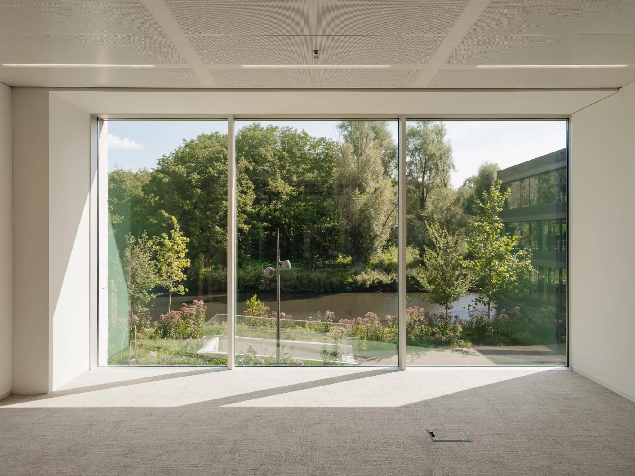 Uitzicht vanuit een modern, leeg kantoor aan de Nachtwachtlaan op een groene tuin met vijver en omliggende bomen.
