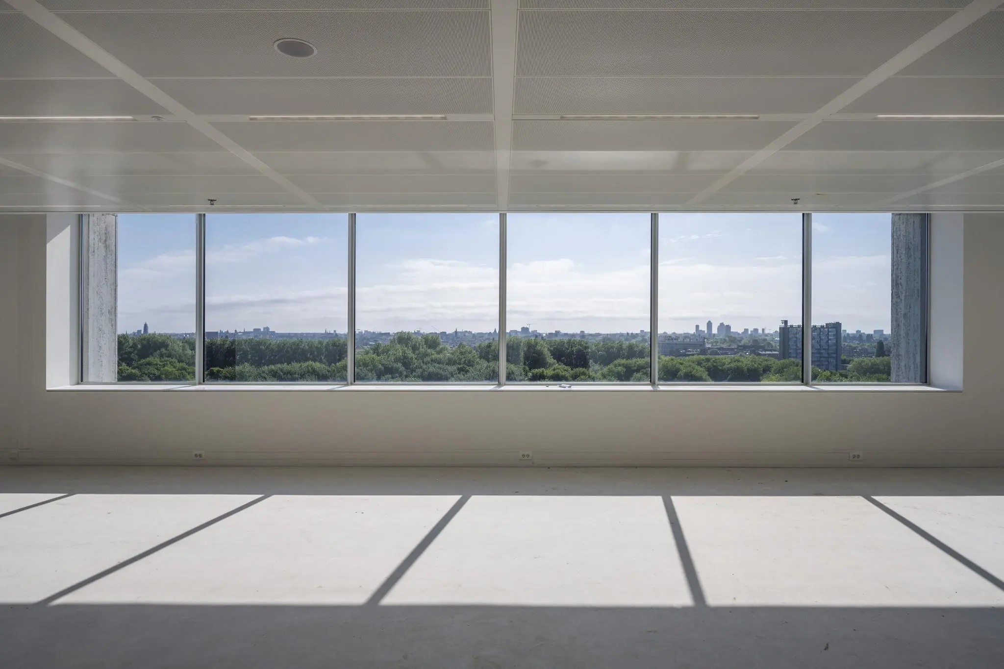 Leeg, modern interieur met grote ramen die uitkijken op een groen stadslandschap aan de Nachtwachtlaan.
