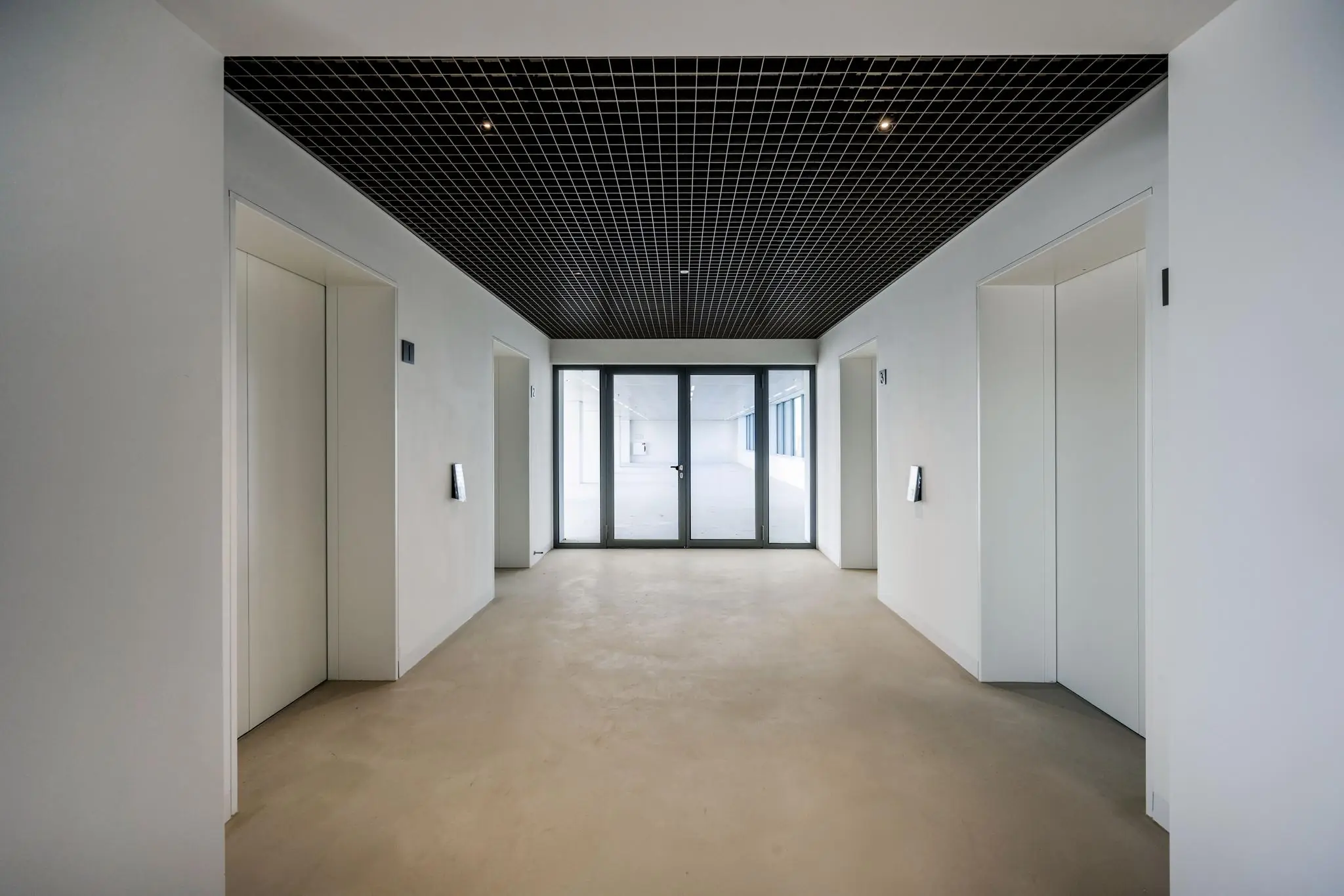 Moderne, minimalistische liftlobby in een kantoorgebouw aan de Nachtwachtlaan met vier liften en glazen deuren naar een open ruimte.