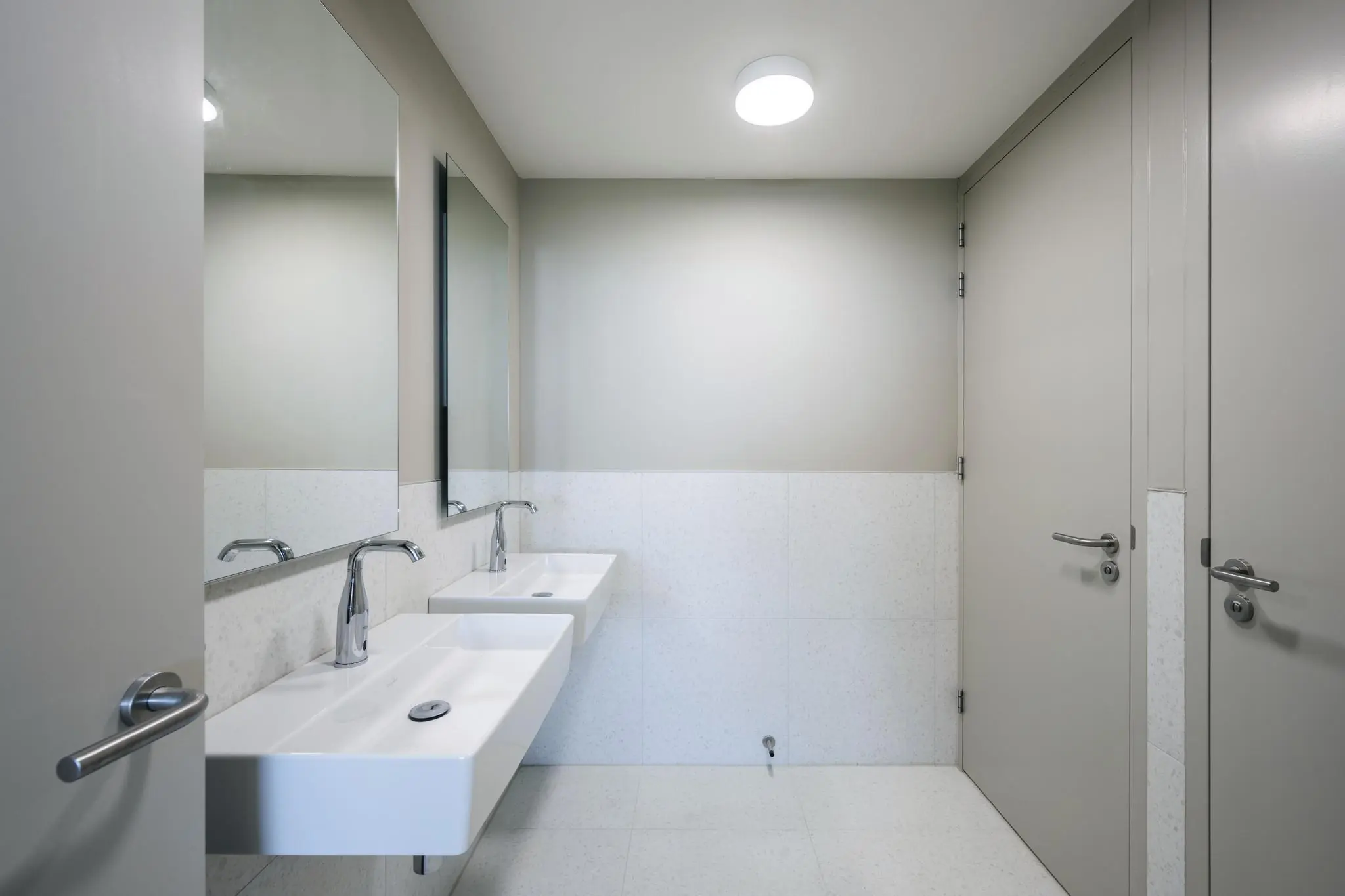 Moderne sanitaire ruimte aan de Nachtwachtlaan met twee wastafels, spiegels en lichtgrijze deuren.