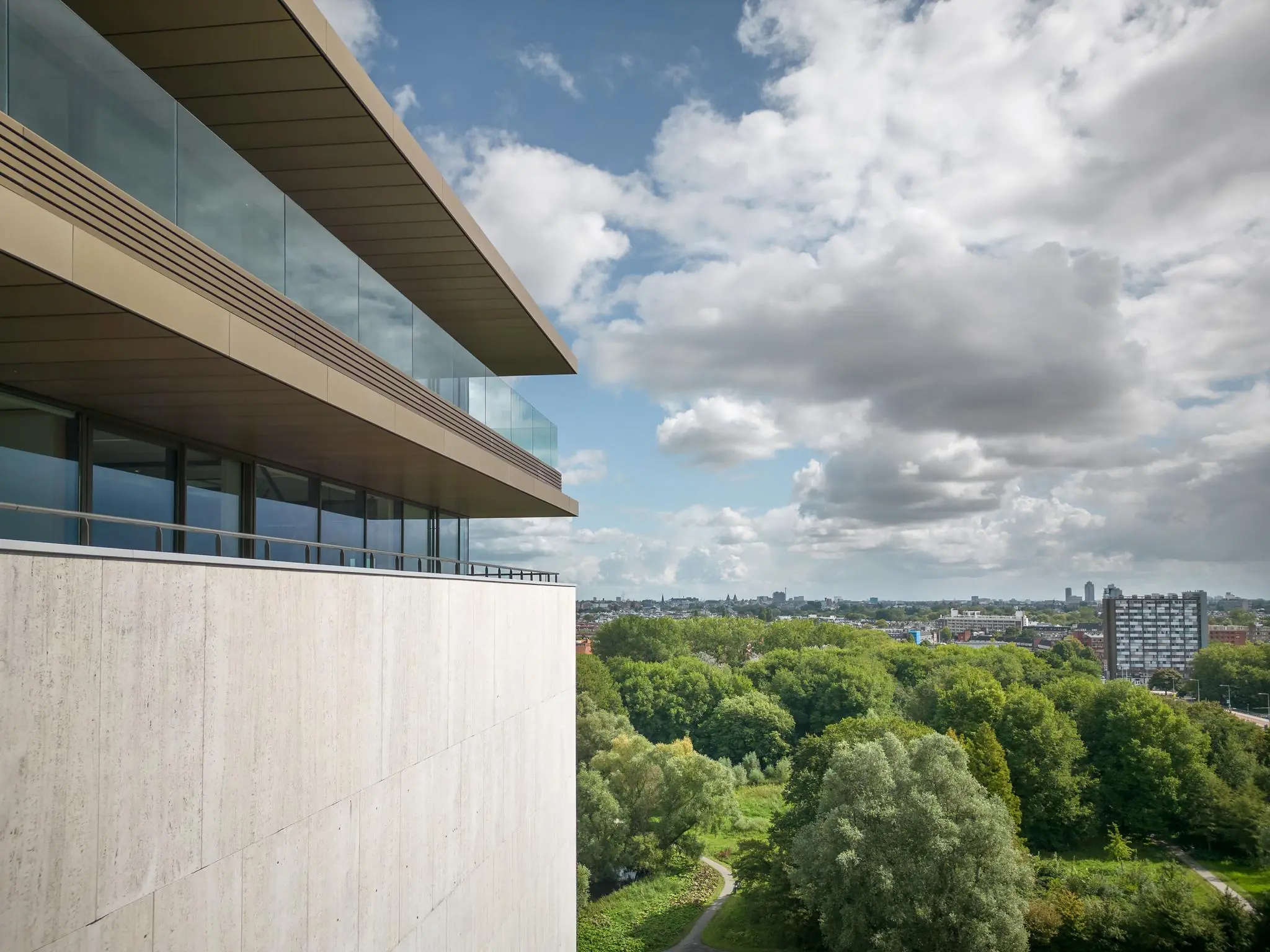 Uitzicht vanaf een modern gebouw aan de Nachtwachtlaan op een groen stadslandschap onder een deels bewolkte hemel.