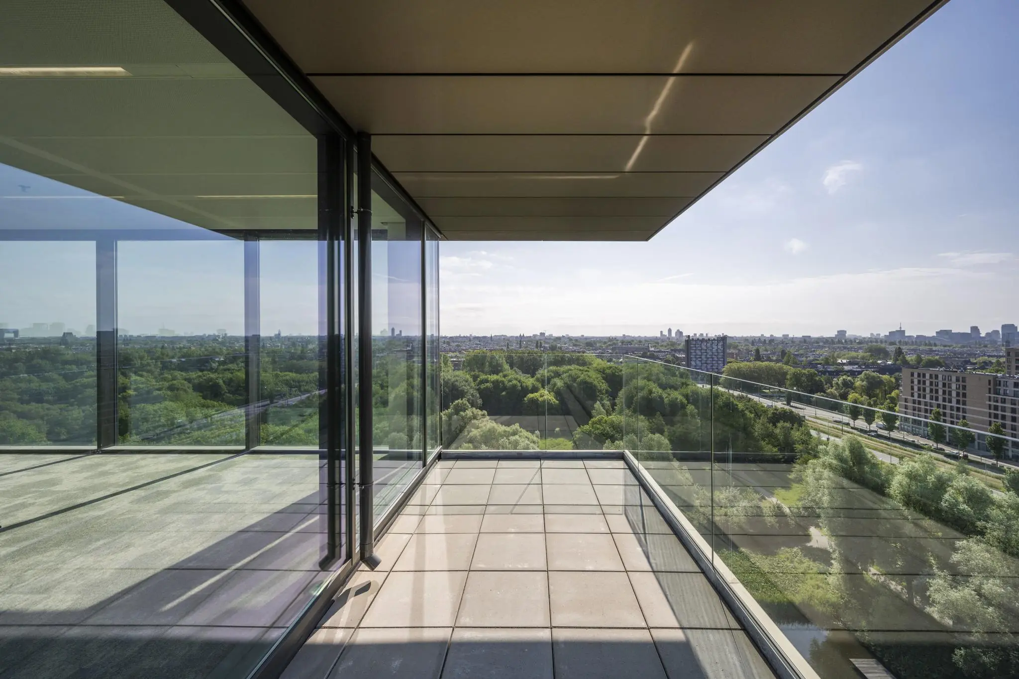 Glazen balkon met uitzicht op het groen en de stad vanaf een hoog gebouw aan de Nachtwachtlaan.