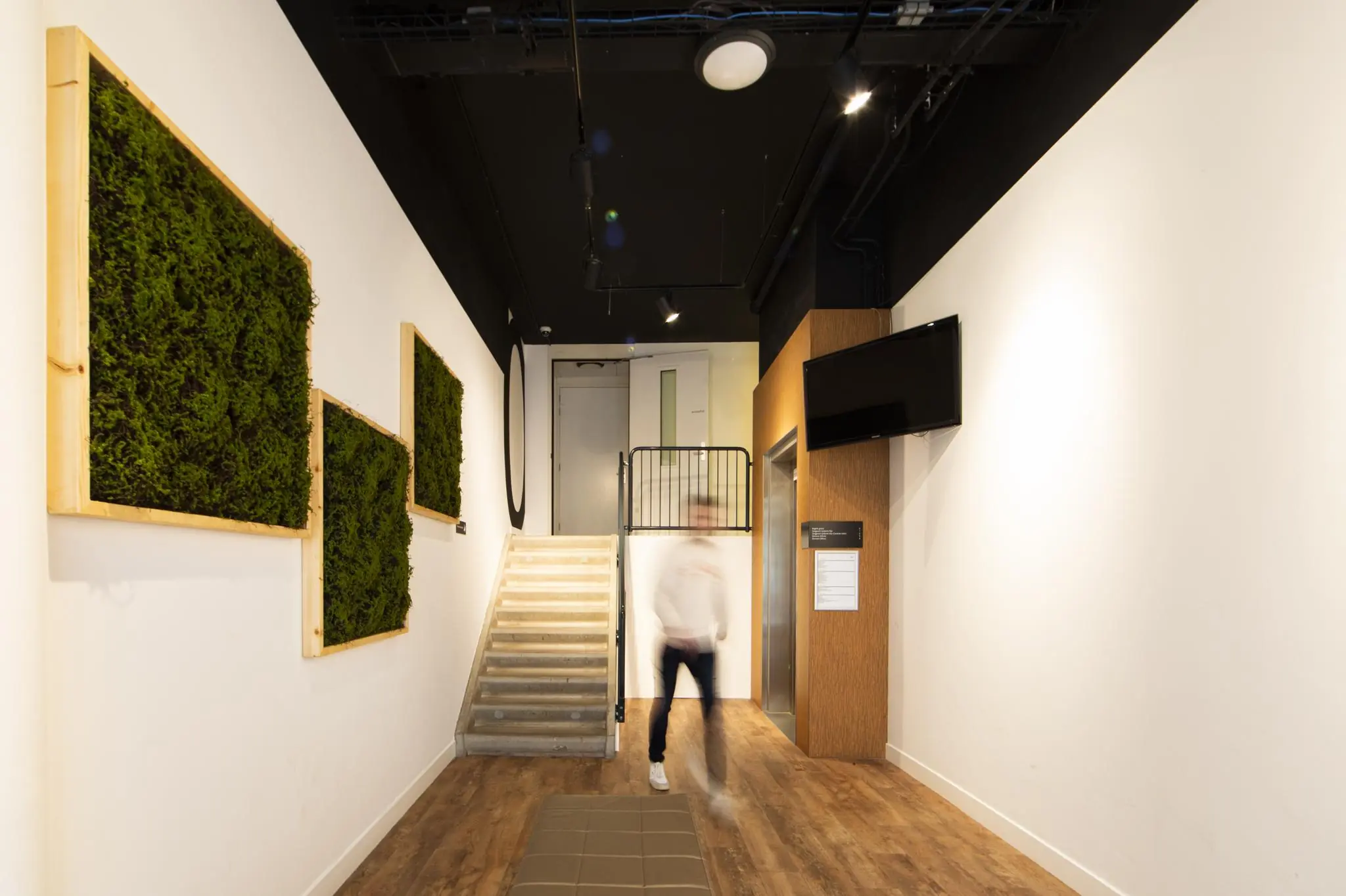 Moderne entreehal van Middenburcht met trap, lift, verticale groene wanddecoratie en een bewegende persoon.